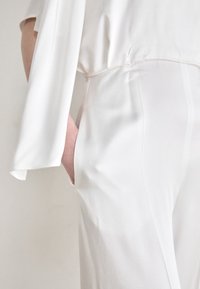 White, lightweight fabric with a flowing design, featuring a loose sleeve and side pockets in a smooth, streamlined shape.