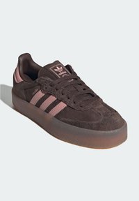 Brown suede Adidas Samba sneaker with pink stripes, gum sole, and logo on tongue, photographed against a light background.