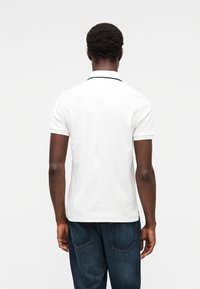 Λευκό κοντομάνικο πόλο μπλουζάκι, στενή γραμμή, με αντίθετη σκουρόχρωμη επένδυση για το γιακά, φορεμένο με σκούρο μπλε τζιν. Απλός σχεδιασμός με ελάχιστες λεπτομέρειες.