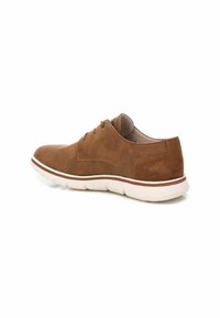 Zapato de ante marrón con punta redondeada, que cuenta con un upper suave, suela de goma blanca y detalles de costura mínimos en la parte trasera y los lados.