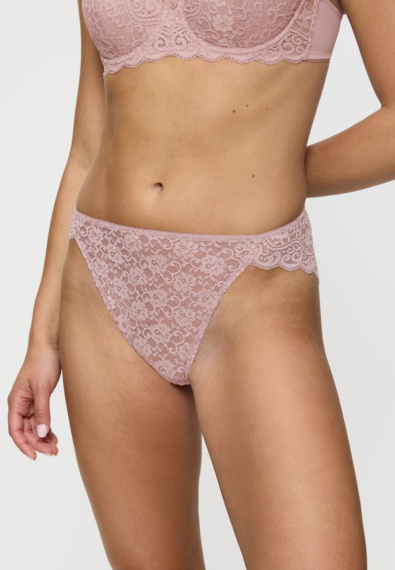 Koronkowe stringi w delikatnym różu z kwiatowymi wzorami, falistymi krawędziami i lekką, delikatną fakturą. Zaprojektowane z myślą o komforcie i stylu.