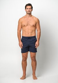 Marinblå simshorts tillverkade i ett lätt material, med elastisk midja och dragsko, slät yta och längd ovan knäna.