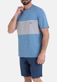 Chemise bleu clair à manches courtes avec une rayure horizontale grise, dotée d'une patte de boutonnage à trois boutons et d'un petit logo. Associée à un short bleu marine.