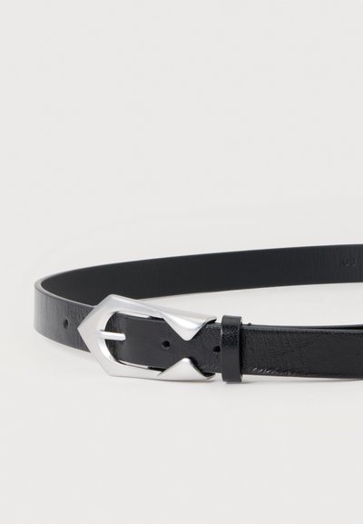 Ceinture en cuir noir avec une boucle géométrique argentée et brillante, posée sur une surface blanche unie. Aucun autre objet ou personne n’est présent.