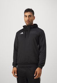 Schwarzer sportlicher Hoodie mit einem Halb-Reißverschluss-Kragen, ausgestattet mit einem strukturierten Brustpanel und drei weißen Streifen an den Ärmeln, aus weichem Stoff gefertigt.