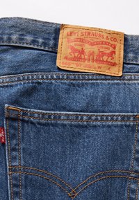 Dunkelblaue Jeans aus Denim mit einem Lederetikett, das roten Text und Pferdegrafiken zeigt. Charakteristische Stickerei an der Gesäßtasche und genietetes Design.
