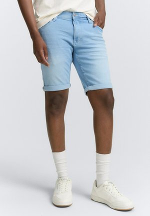Shorts di denim azzurro chiaro con risvolti, tasche anteriori e un aspetto sbiadito, abbinati a sneaker bianche e calze.