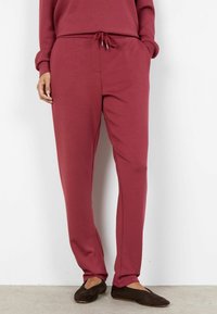 Bordowe spodnie dresowe wykonane z miękkiego materiału, wyposażone w regulowany sznurek w talii, boczne kieszenie oraz zwężany krój nogawek.