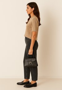 Beige gebreide top met korte mouwen, hoge zwarte jeans, zwart leren handtas met een gouden gesp, en zwarte loafers.