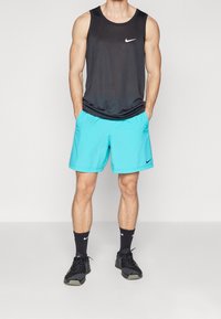 Débardeur de sport noir sans manches, short turquoise et chaussures de sport noires avec des accents blancs. Logo Nike distinctif sur le débardeur et le short.