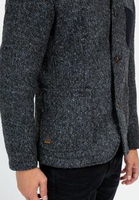 Gestructureerde donkergrijze cardigan met blauwe spikkels, met een knoopsluiting aan de voorkant, een patchzak en een logo-label aan de onderkant.