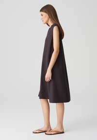 Mouwloze zwarte linnen jurk met een losse pasvorm, knie-lengte, ronde halslijn en zij-splitten, gecombineerd met bruine platte sandalen.