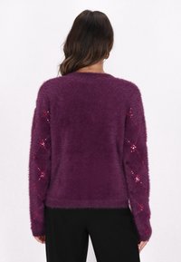 Suéter púrpura de peluche con un acabado texturizado, que presenta patrones de diamantes embellidos en las mangas. Cuello redondo simple y ajuste ceñido.