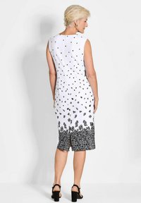 Ärmelloses weißes Kleid mit schwarzen Blumen- und Punktmustern, knielang, mit einem gespaltenen Saum und einem dezenten Reißverschlussdetail hinten.