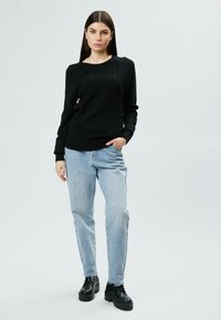 Pull en tricot noir avec motif en torsades, col rond, manches longues ; associé à un jean bleu clair à coupe décontractée et des chaussures à plateforme noires.