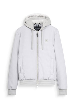 Veste à capuche zippée en quilt léger gris clair avec cordons de serrage, deux poches avant, des poignets côtelés et un petit logo AM brodé sur la poitrine.