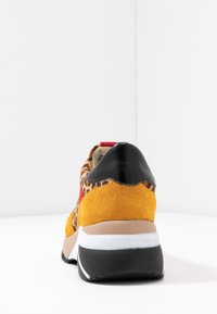 Sneakers med leopardmönster, en gul mockaovandel, röda detaljer och en svart läderklack. Har en vit mellansula och en beige yttersula.