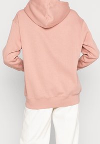 Pink hooded sweatshirt with a relaxed fit, soft texture, and ribbed cuffs. Features a kangaroo pocket and a clean, minimalist design.