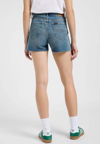 Jasnoniebieskie szorty dżinsowe z postrzępionym dołem, pięcioma kieszeniami i wysokim stanem, w połączeniu z zielono-białymi trampkami i białymi skarpetkami.