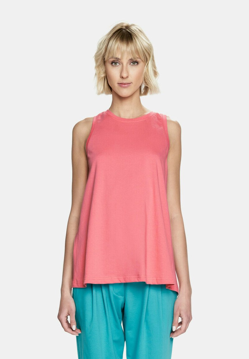 Top bez rękawów w miękkim koralowym kolorze, luźny krój z okrągłym dekoltem, w połączeniu z luźnymi turkusowymi spodniami. Gładka tekstura, minimalne detale.