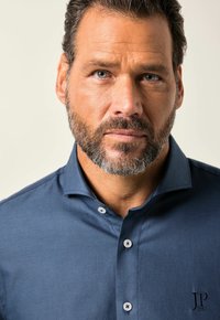 Camicia button-up blu navy con una trama testurizzata, dotata di colletto aperto e ricamo del logo vicino all'orlo, con bottoni di colore chiaro.