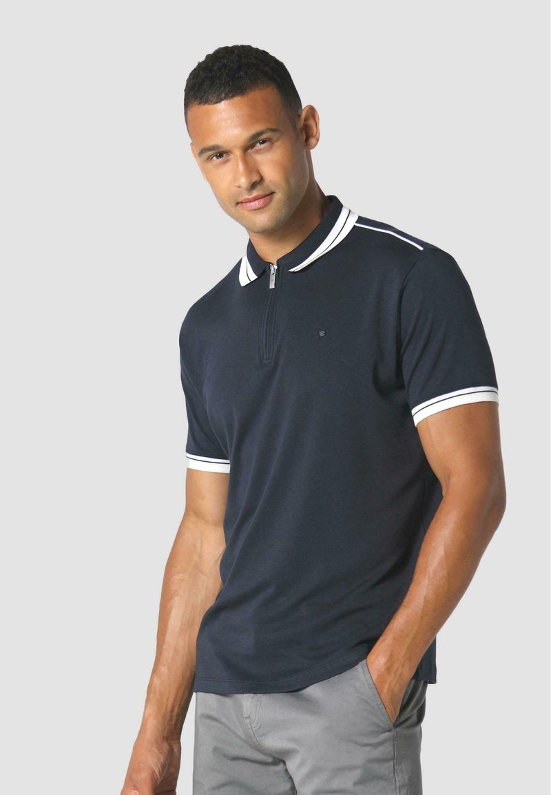 Polo shirt blu navy con colletto zip, dettagli a righe bianche sulle maniche, maniche corte e un design aderente per un look moderno.