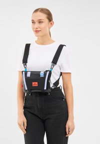 Svart axelremsväska med blå och lila accenter, tillverkad av glänsande material. Har justerbara remmar och en djärv röd logotyp på framsidan.