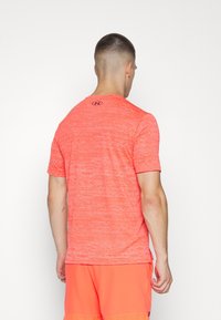 Kortärmad sporttröja i livlig korallfärg med en strukturerad mönstring och logotyp på baksidan, tillverkad av fukttransporterande material.