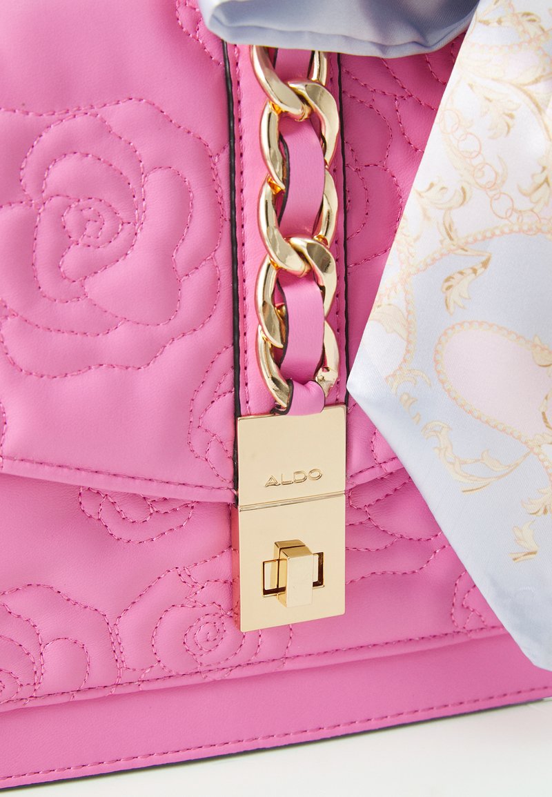 Różowa pikowana torebka wykonana ze skóry, z złotym łańcuszkiem, złotym zapięciem z logo marki oraz dołączonym wzorzystym szalikiem.