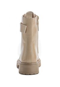 Bottines à talon en vernis beige avec une texture lisse, fermeture éclair à l'arrière et un détail de sangle. Semelle en caoutchouc épaisse avec un design strié.