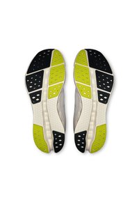 Running shoes with a white upper, textured light gray accents, and a sole featuring black, yellow, and green rubber sections and patterned details.