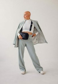 Světlé zelené kalhoty na míru s odpovídajícím sakem, bílé žebrované svetr a černá crossbody taška s prošívaným designem. Bílé tenisky.