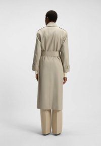 Beiger Trenchcoat mit tailliertem Gürtel, langen Ärmeln und Schulterklappen; glattes Material mit einer passgenauen Passform. Die Hose hat weite Beine.