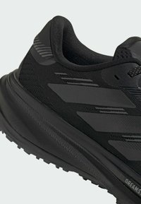 Sort atletiksko med overdel i tekstureret stof, der har matte og blanke stribede detaljer samt en tyk, rillerig gummisål.