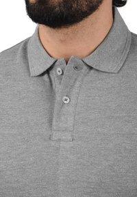 Grå polo t-shirt med en blød tekstur, der har en krave og to knapper. Stoffet ser let tekstureret ud med et subtilt heather-mønster.