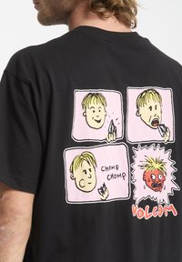 Camiseta de algodón negra con un gráfico de cartoon en la parte de atrás que presenta cuatro paneles que representan a un personaje comiendo, con texto y acentos coloridos.