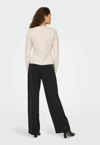 Pull en beige clair moulant avec des manches longues, associé à un pantalon large noir taille haute. Texture subtile et design épuré.