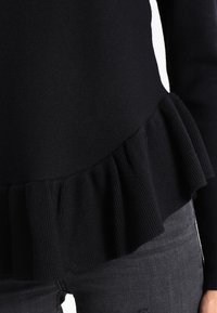 Zwart gebreid sweater met een geribbelde, gefronste zoom. Lange mouwen en een getailleerd lijfje, gemaakt van zachte, textuurstof.