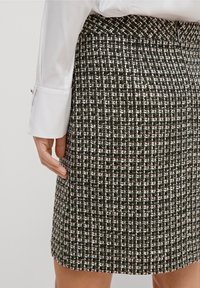 Jupe tissée noir et blanc avec un motif texturé. Ceinture plate et coupe à hauteur du genou. Accompagnée d'un chemisier blanc à manches longues.