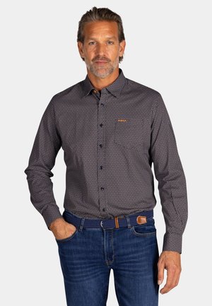 Langsleeve knoopshirt in marineblauw met witte stippen, met een kraag en knopen aan de voorkant; gecombineerd met blauwe jeans en een bruine riem.