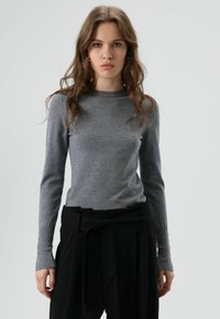 Grijze lange mouwen trui met een getailleerd ontwerp, geribbelde halslijn en knoopdetails op de mouwen, gecombineerd met hoge taille zwarte broek.