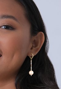 Guldørering med en hængende design, der har en stor perle og farverige perler i et gradientmønster. Glat tekstur, elegant form.