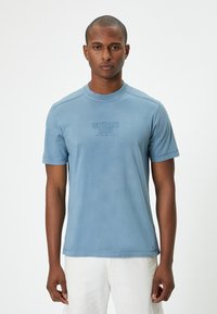 Hellblaues Kurzarm-T-Shirt mit Rundhalsausschnitt, das einen dezenten Druck auf der Vorderseite zeigt. Weicher Stoff und lockere Passform, einfaches Design.