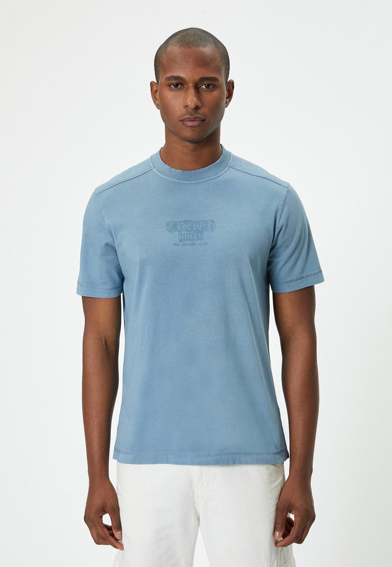 Hellblaues Kurzarm-T-Shirt mit Rundhalsausschnitt, das einen dezenten Druck auf der Vorderseite zeigt. Weicher Stoff und lockere Passform, einfaches Design.