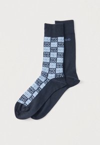 Granatowe skarpetki z powtarzającym się wzorem "HUGO" w jasnoniebieskich i ciemnoniebieskich kwadratach. Wykonane z miękkiego, elastycznego materiału.
