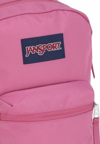 Roze Jansport rugzak met een voorvak met rits en een marineblauw logopatch op duurzame stof.