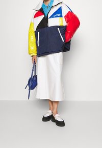 Colorful puffer jacket in blue, red, yellow, and black; white skirt; black and white slip-on shoes; blue handbag with a structured design.