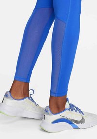 Leggings deportivos azules con un panel de malla. Zapatillas de running blancas y azules con detalles en negro y una suela texturizada.