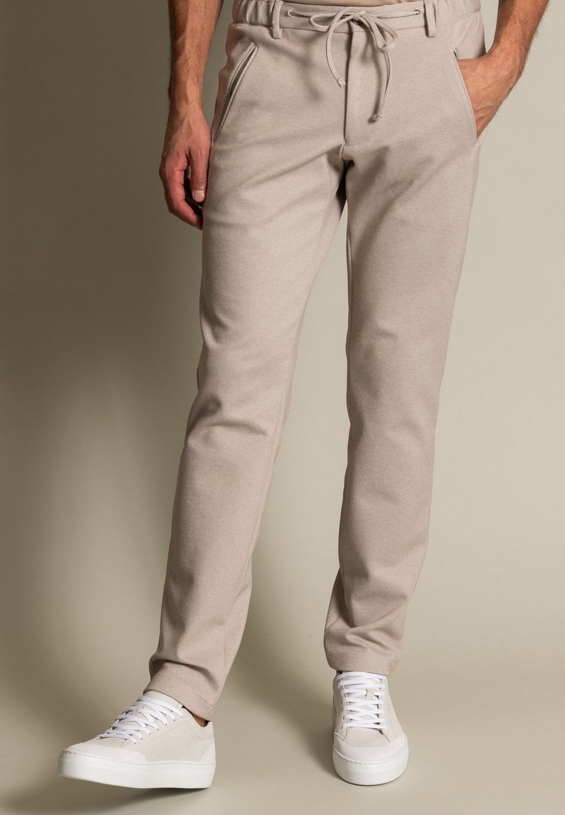 Beige Jogginghosen mit einem Kordelzugbund und Seitentaschen, aus weichem Stoff, kombiniert mit weißen Schnürsneakern.