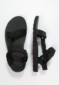 Sandalias negras con suelas de goma texturizadas y correas de nailon ajustables en el pie y el tobillo. Presentan un diseño plano sin adornos.